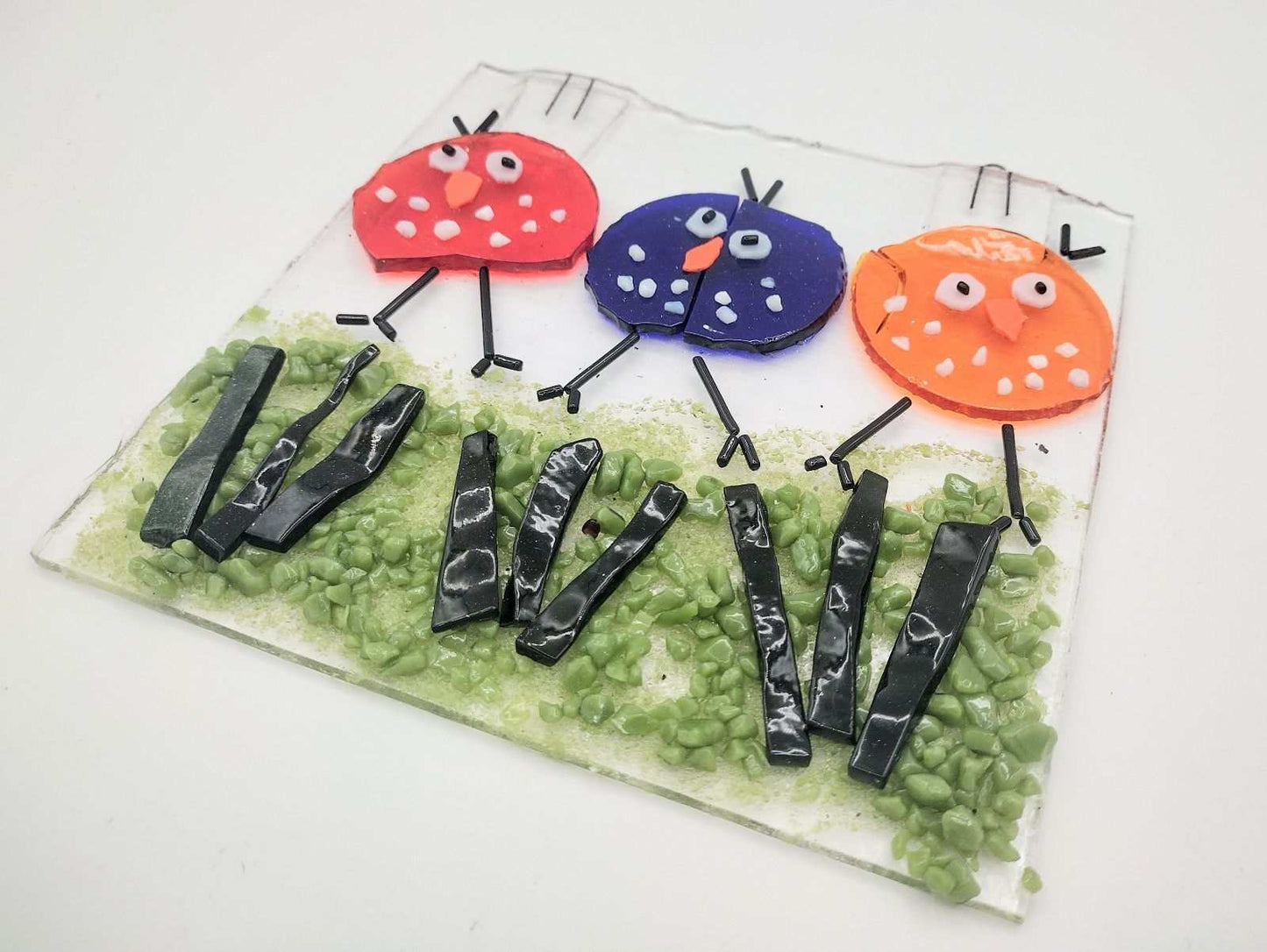 Colorful fused glass artwork featuring three stylized birds on green grass made in Choose Your Own Fusing Project class