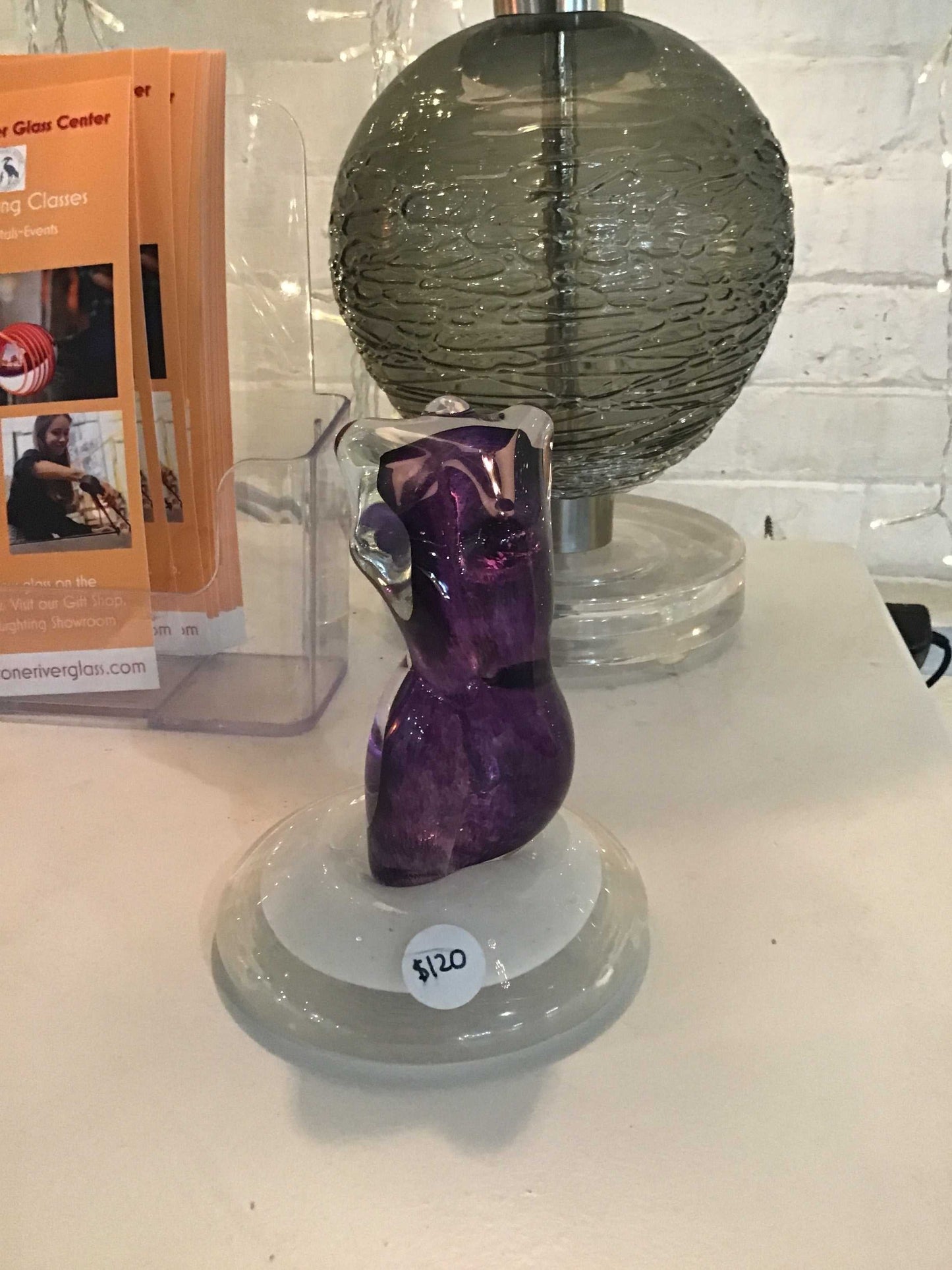Purple glass sculpture of a lady torso displayed on a clear round base with a $120 price tag.