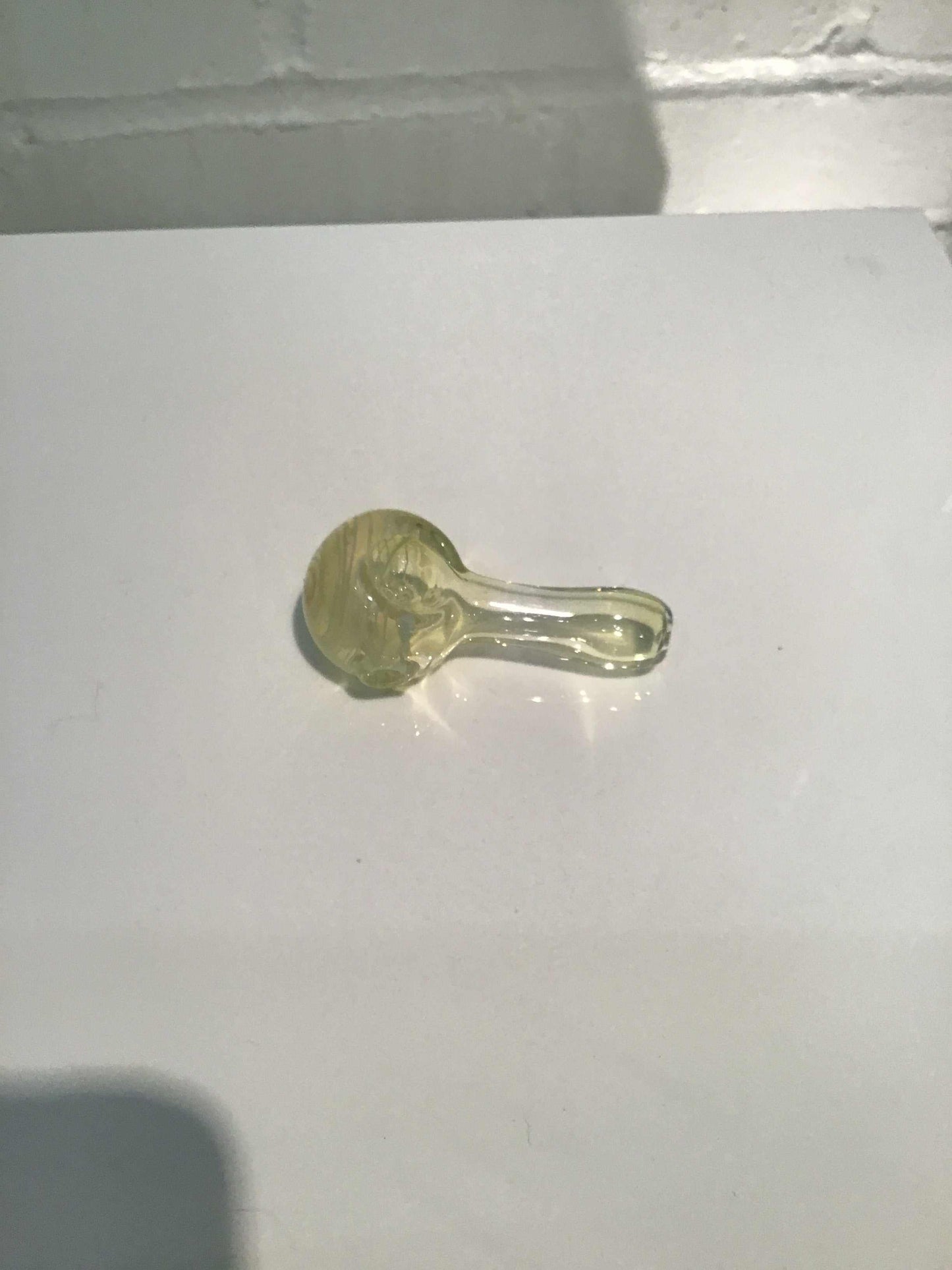 Mini pipe made of translucent glass with a rounded bowl and short stem placed on a white surface