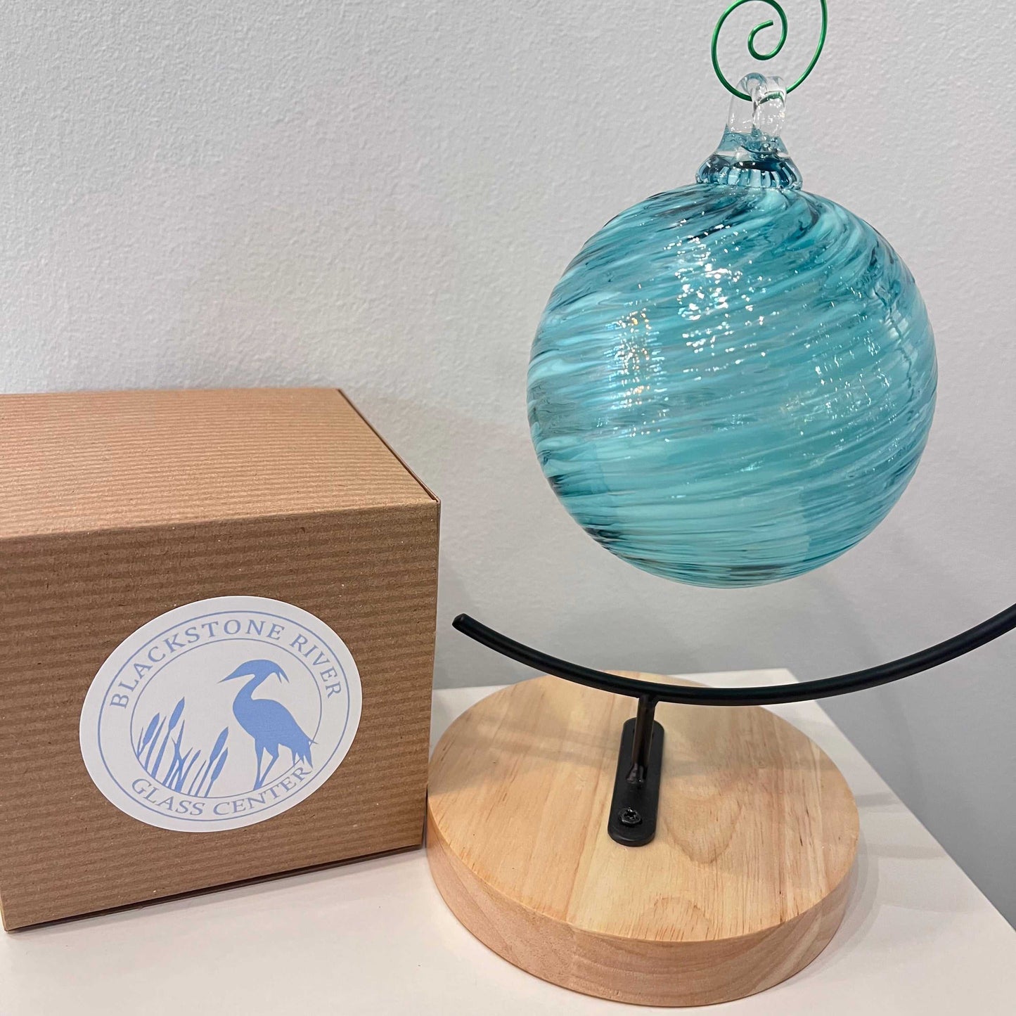 AquaCeledon Optical Glass hand-blown contemporary glass piece with aqua and celedon tones suspended on wooden stand with Blackstone River Glass Center box