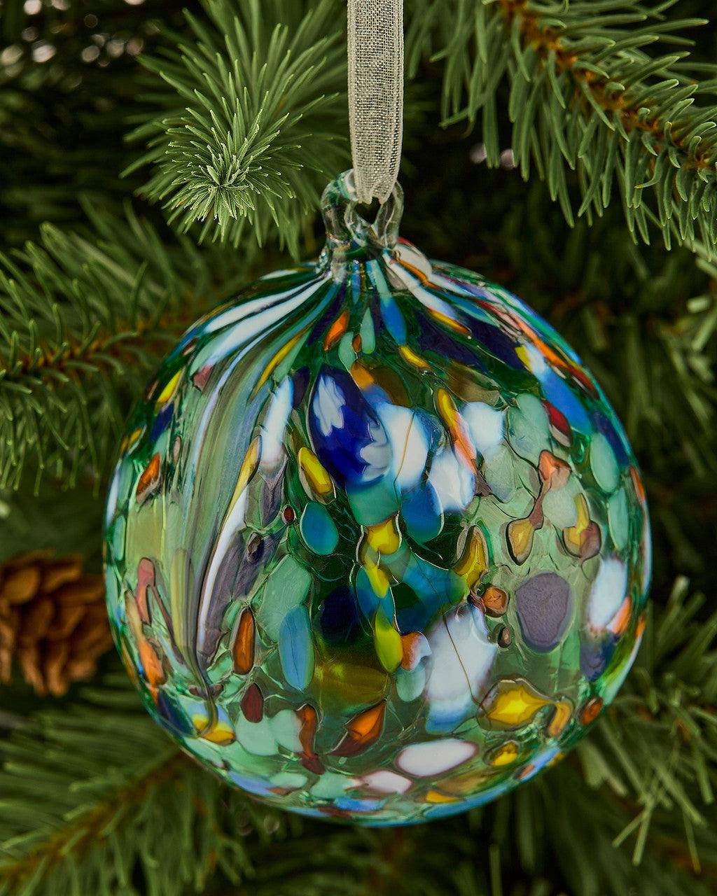 Colorful blown glass ornament hanging on pine tree branch with abstract bubble pattern