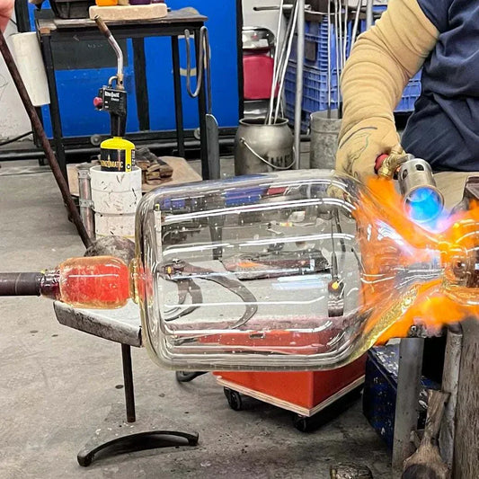 Person shaping a glowing glass vase using a torch in a glassblowing workshop for a Make Your Own Glass Vase class