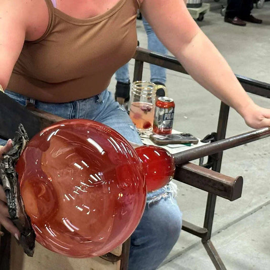 Beginner glass blowing class participant shaping a red glass vase with blowpipe in workshop setting