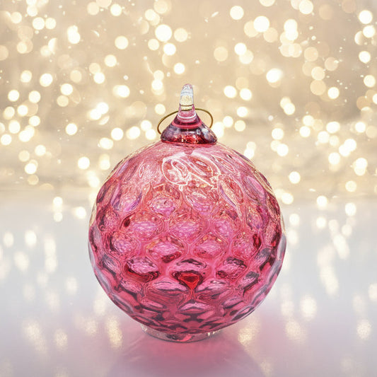 Pink glass ornament with textured surface on a white background