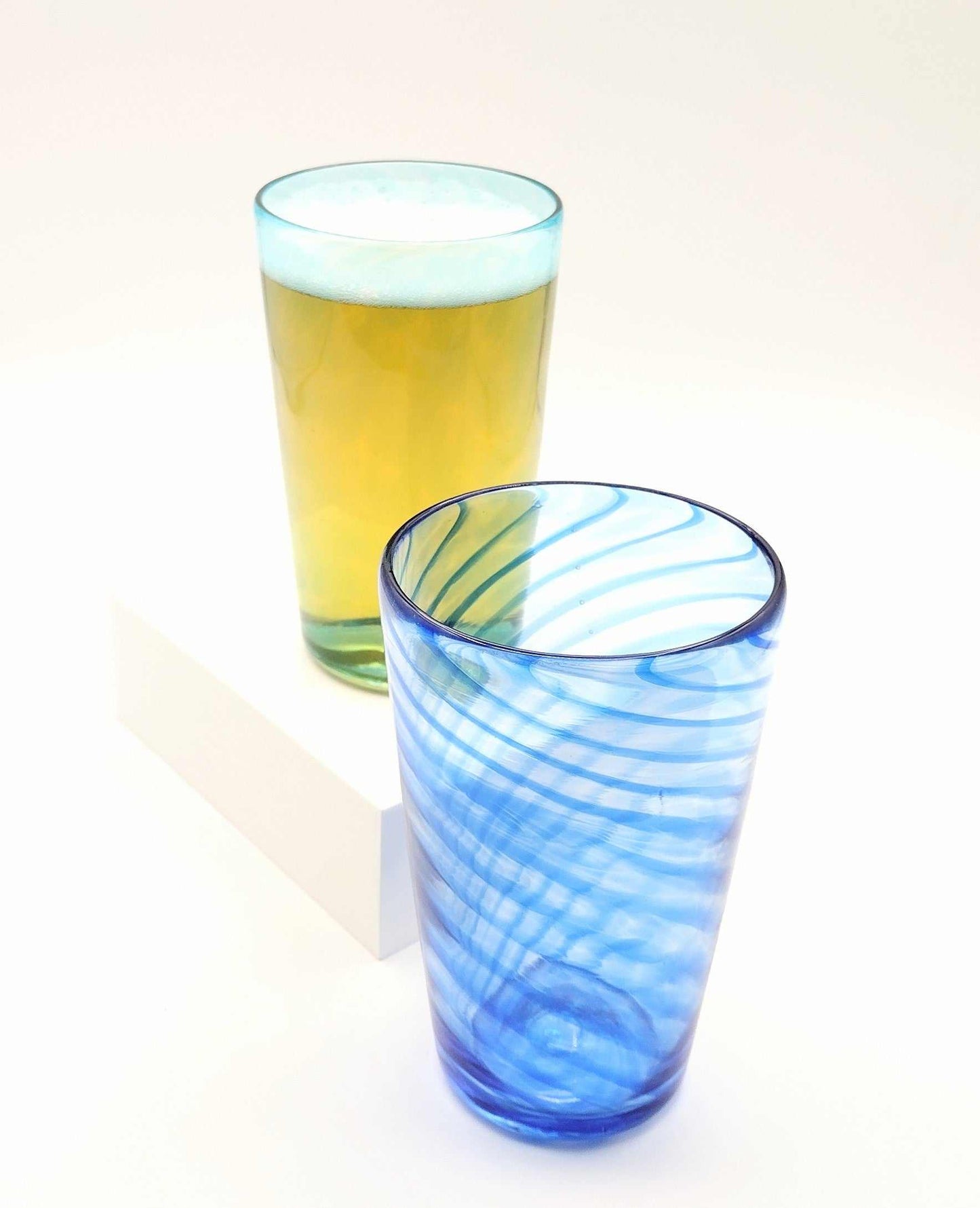 Two handmade drinking glasses for Date Night Glassblowing BYOB class, one filled with beer and one empty blue swirl glass
