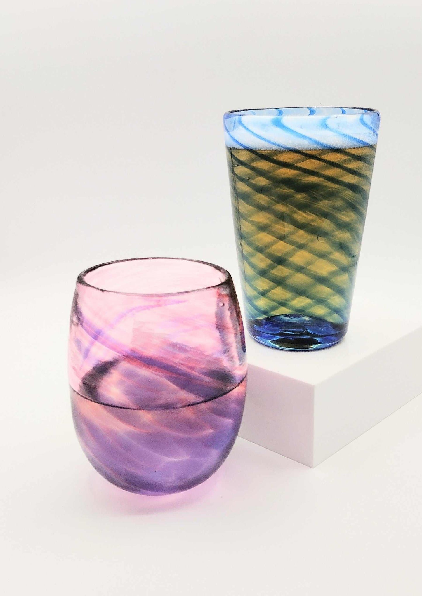 Two hand-blown glass drinking glasses with swirling patterns in blue and purple, displayed on white surface for Date Night Glassblowing class.
