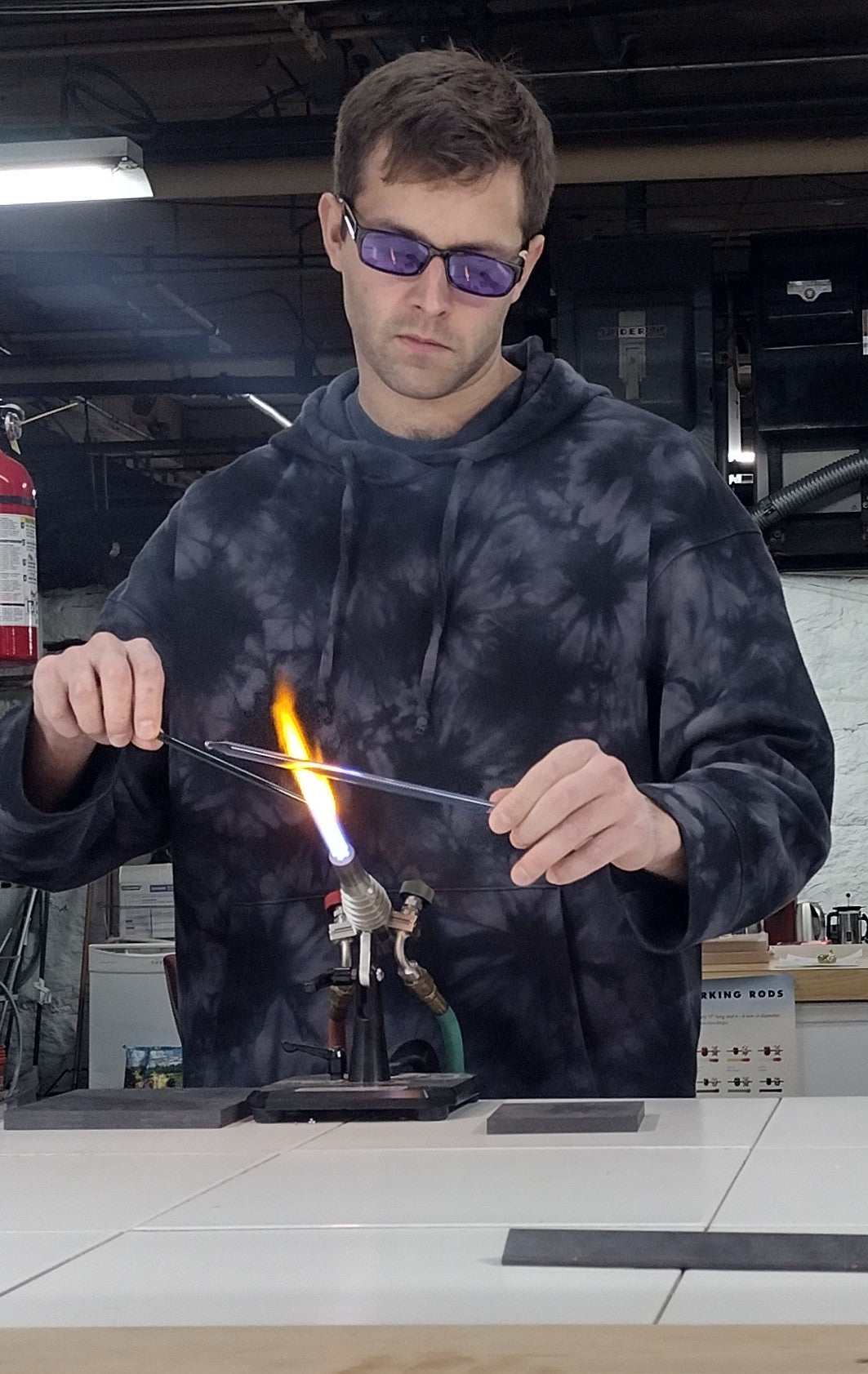 Person wearing protective glasses using a bench torch to heat glass in a flameworking class session