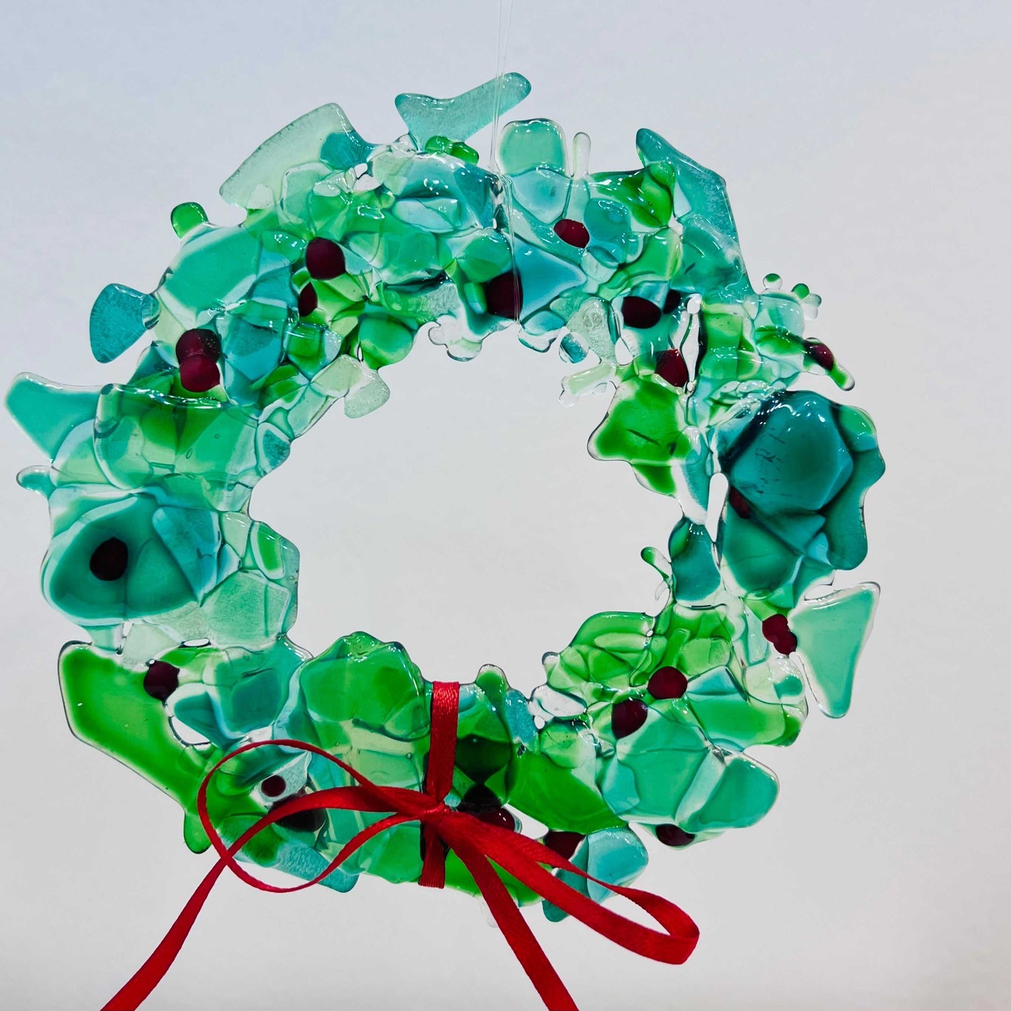 Fused Glass Holiday Wreath with green and blue fused glass pieces and red accents, decorated with a red ribbon bow
