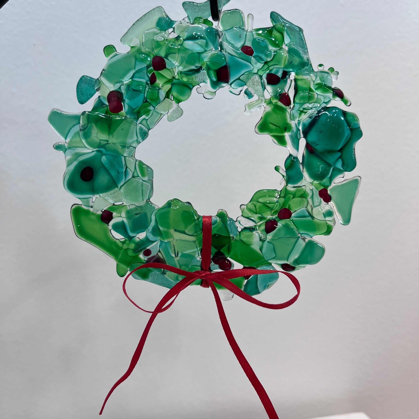 Fused glass holiday wreath with green glass pieces, red accents, and a red ribbon bow, handcrafted for festive décor