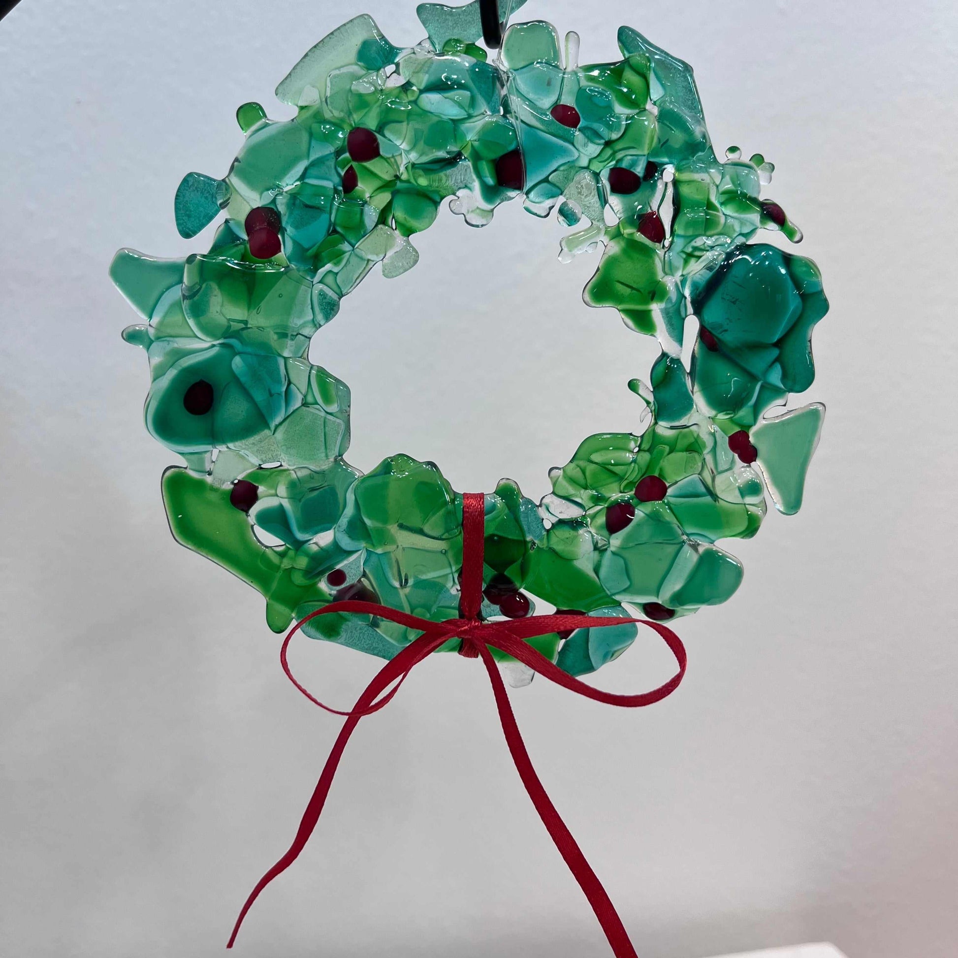 Fused glass holiday wreath with green glass pieces, red accents, and a red ribbon bow, handcrafted for festive décor