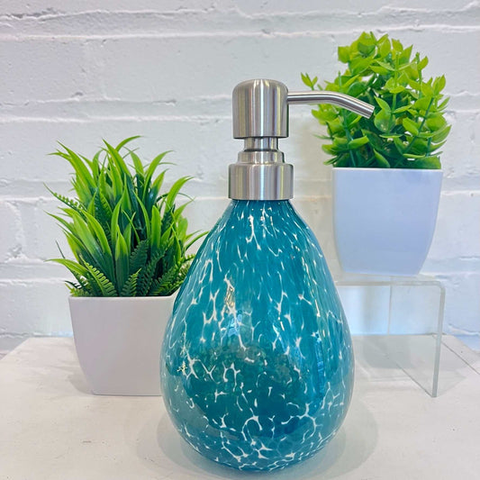 Hand blown glass teal speckled soap dispenser with stainless steel pump next to potted plants