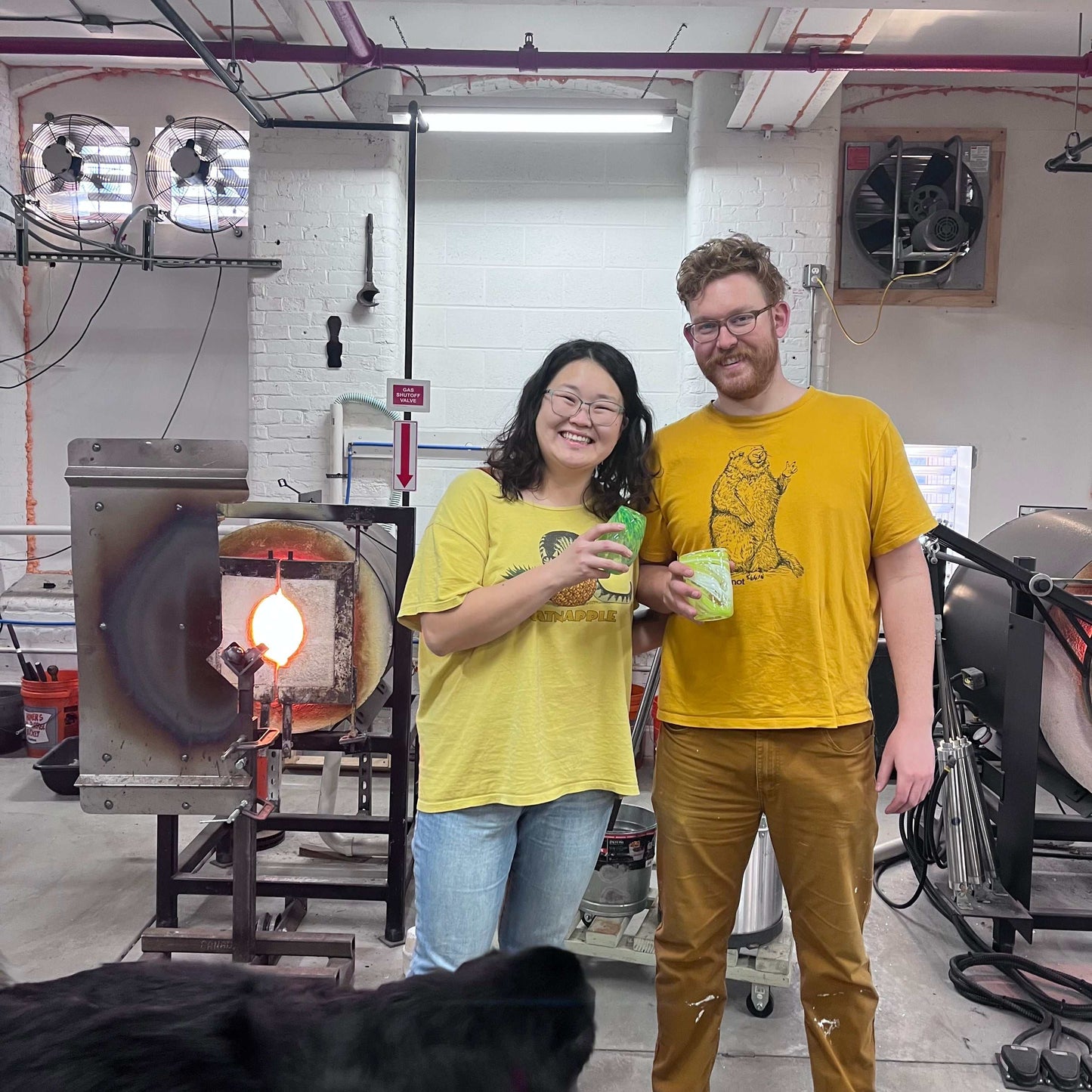 Couple enjoying Date Night Glassblowing class holding their handmade drinking glasses in a glassblowing studio