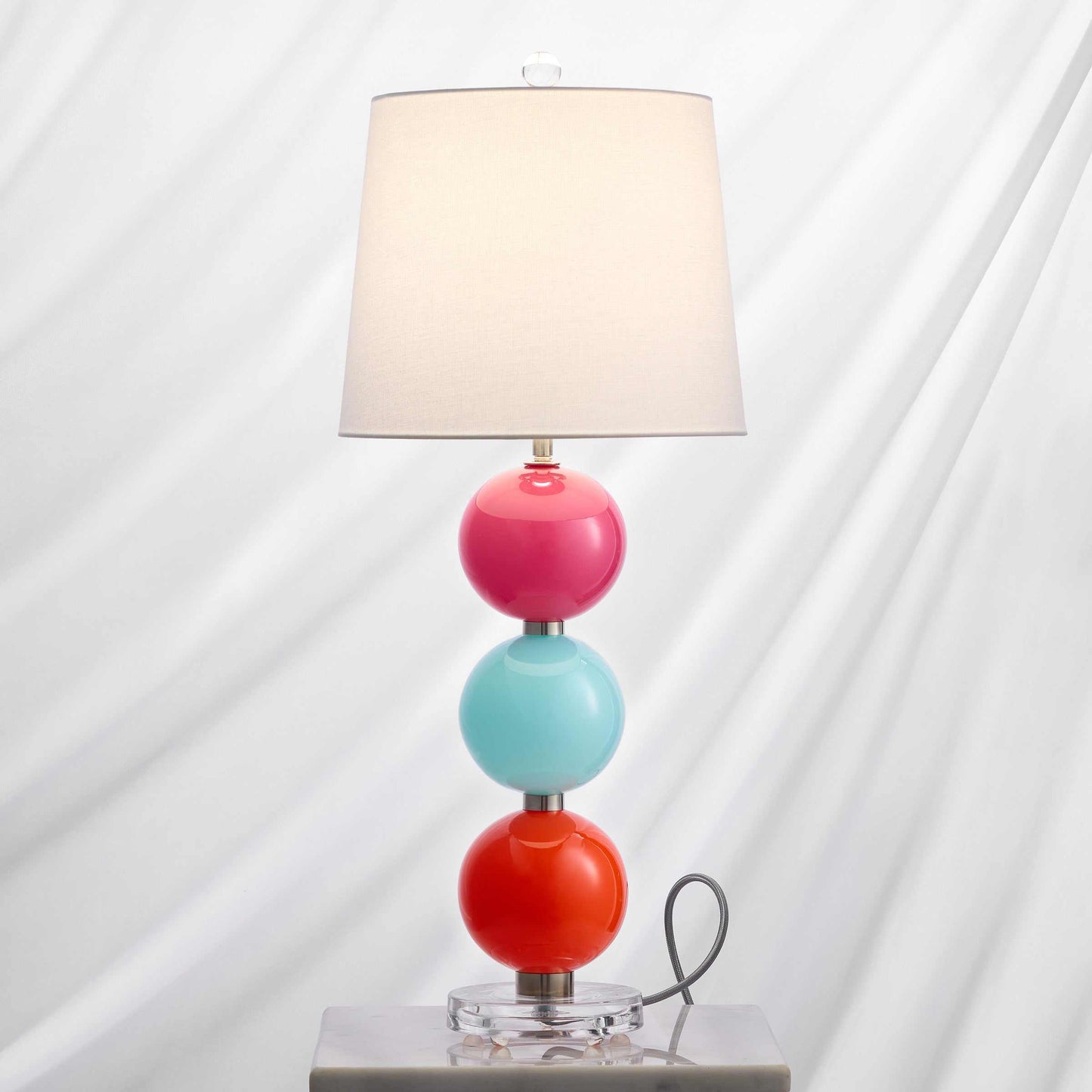 Nina Table Lamp with three colorful stacked glass globes, off-white fabric shade, and silver textile cord with dimmer switch