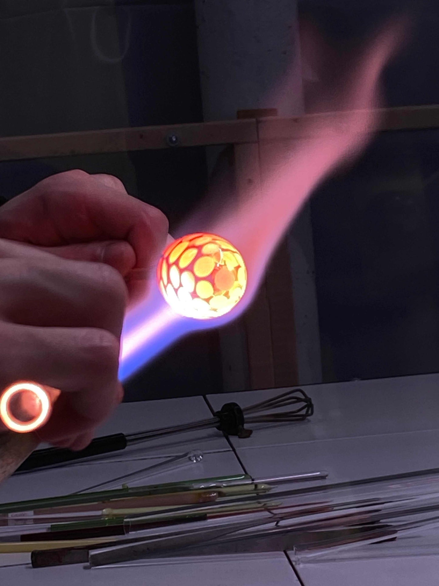 Hands shaping a glowing glass pipe using a flame in a flameworking workshop session