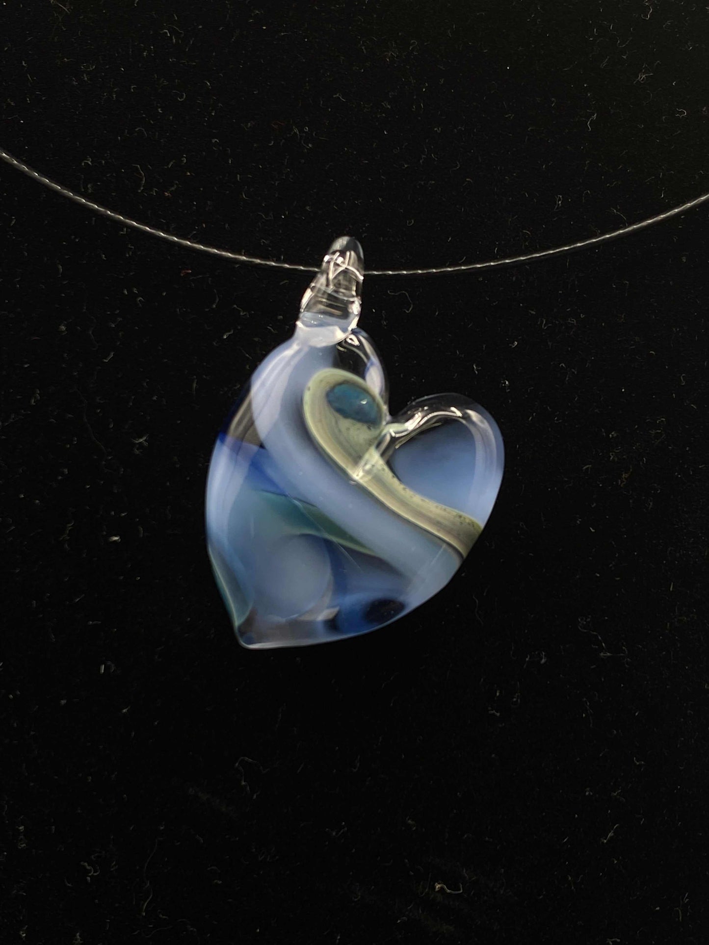 Glass heart pendant with blue and green swirls on a thin wire necklace, showcasing flameworking artistry for a private group glass experience.