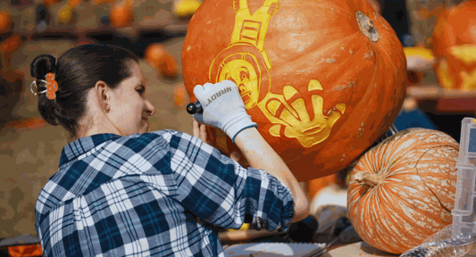 Woman artist carving a detailed design on a large pumpkin at Blackstone River Glass Pumpkin Palooza fall festival
