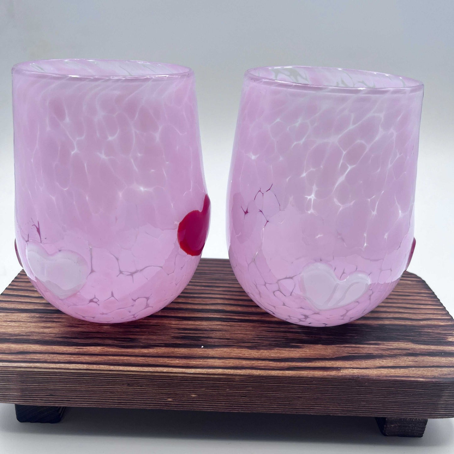 Pair of pink hand-blown Love Cups stemless wine glasses with heart accents on wooden stand