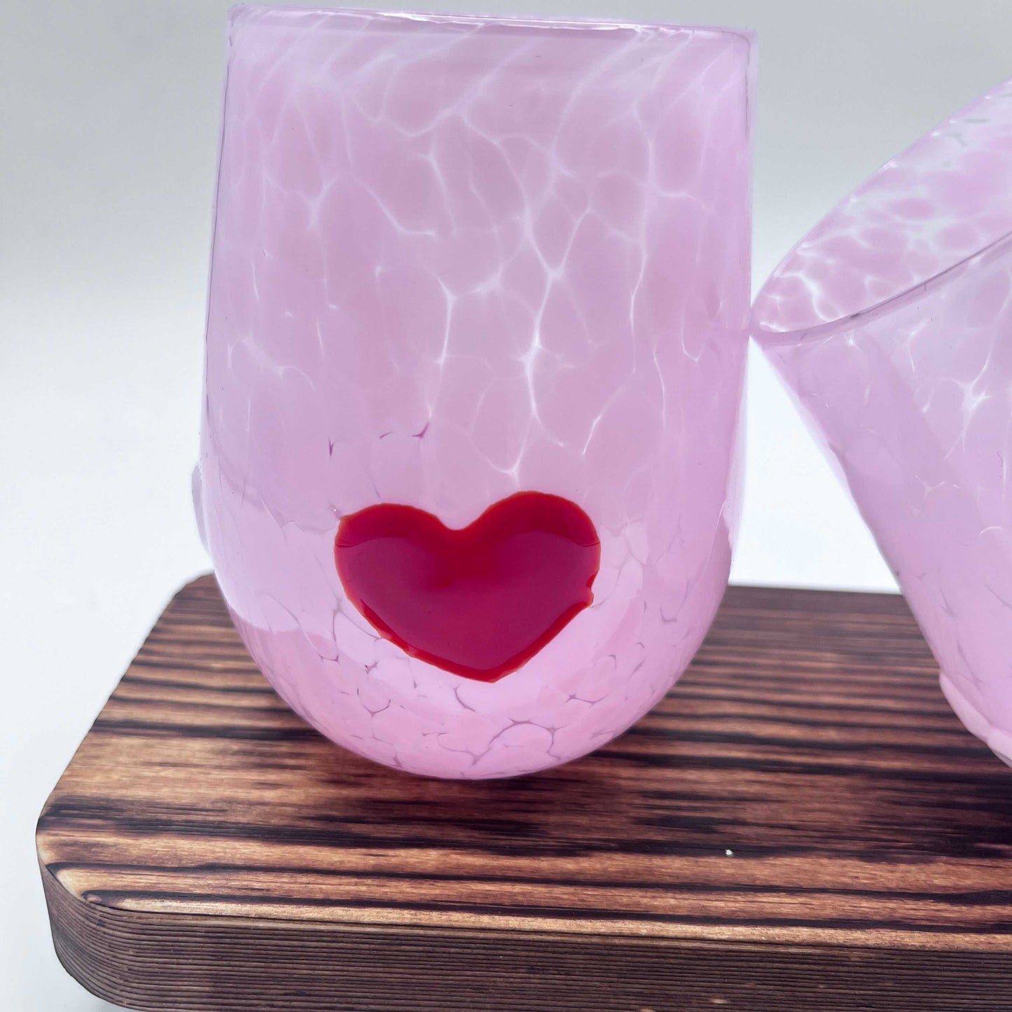 Pink hand-blown stemless wine glass with red heart detail on wooden surface