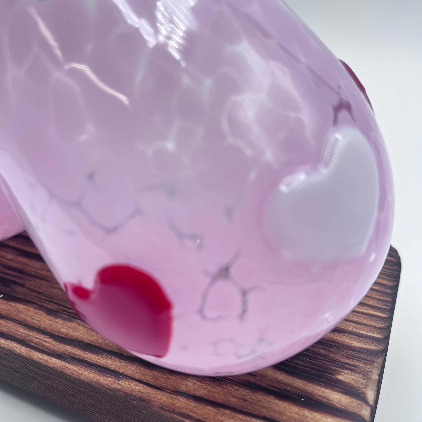Close-up of hand-blown pink Love Cups stemless wine glass with red and white heart accents on wooden surface