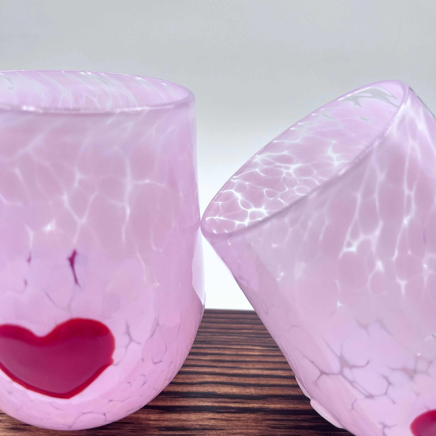 Pair of hand-blown pink stemless wine glasses with red heart accents on wooden surface