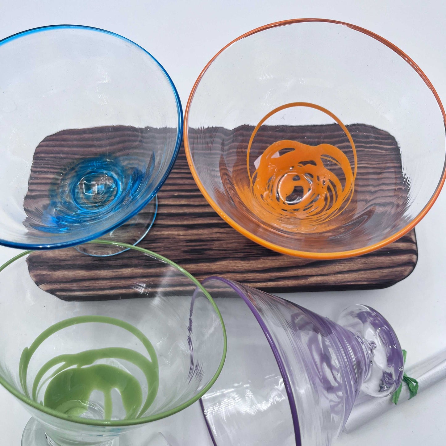Set of colorful hand blown stemless martini glasses with unique swirl designs on wooden serving board