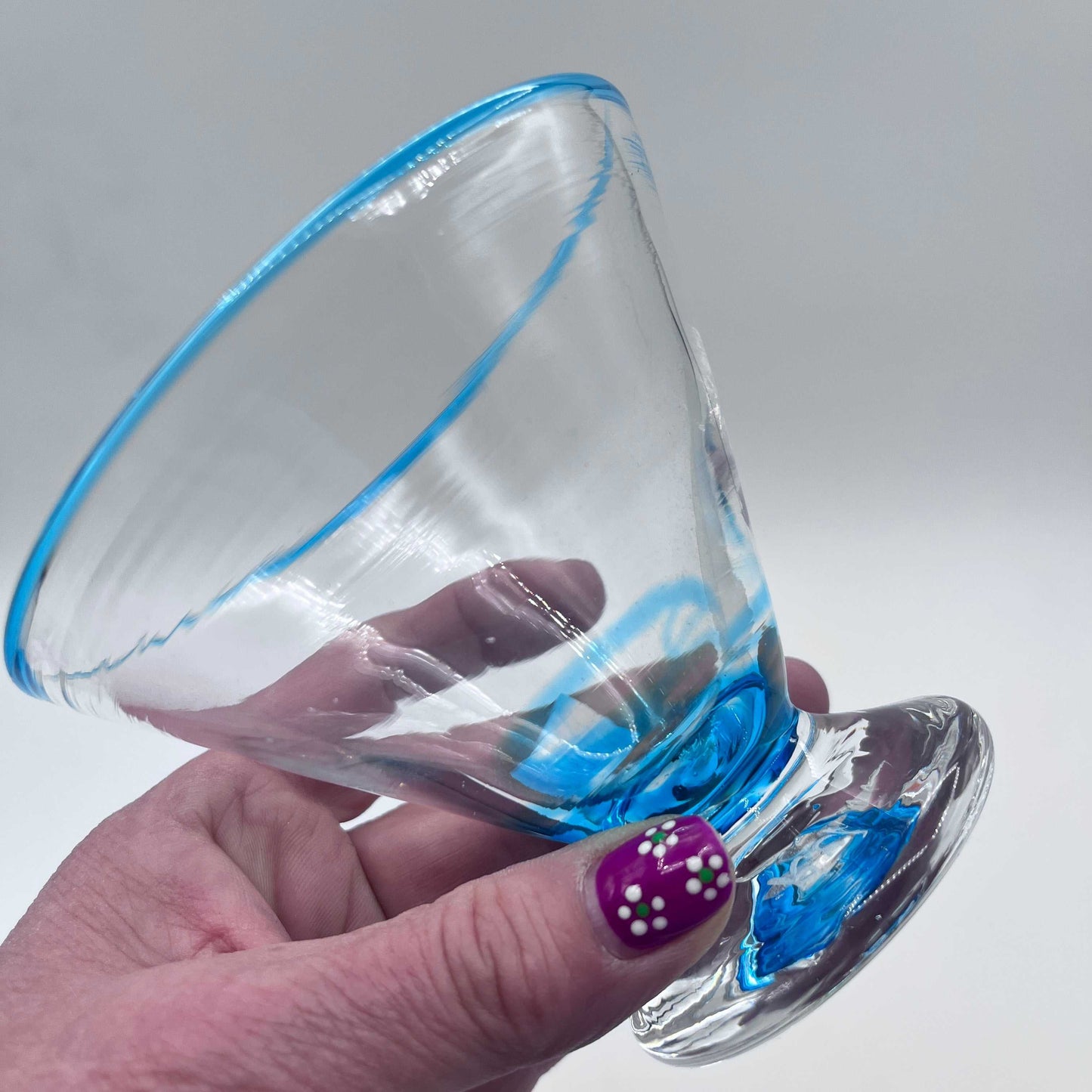 Hand blown stemless martini glass with blue rim, artisan crafted and durable, held in hand