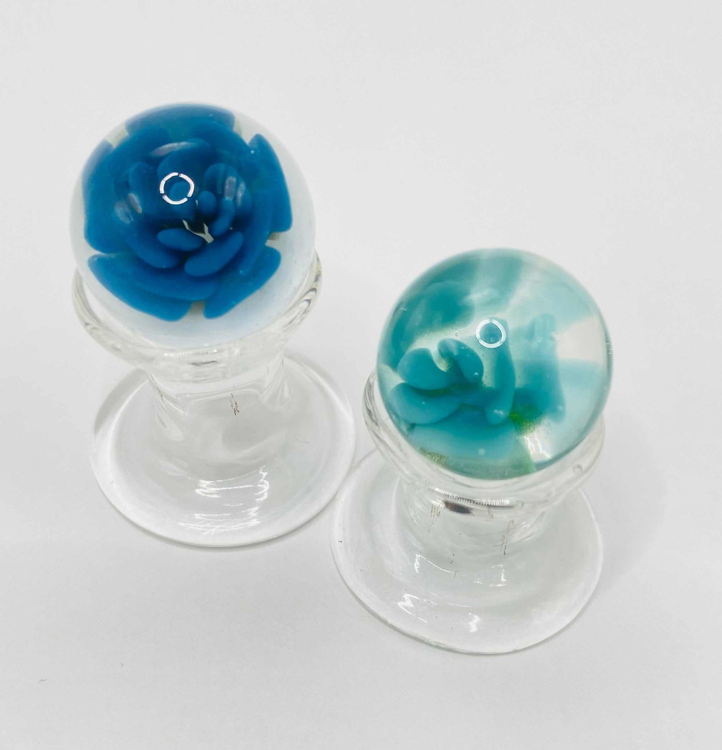 Two handmade glass marbles with blue and turquoise swirls on clear glass stands for Make Your Own Marble craft project