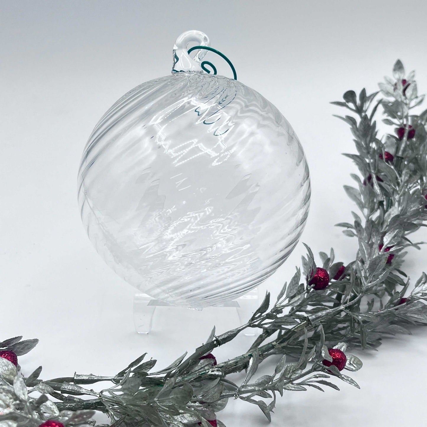 Clear hand blown glass ornament with spiral twist design, 4x4 inches, displayed with festive greenery and red berries.