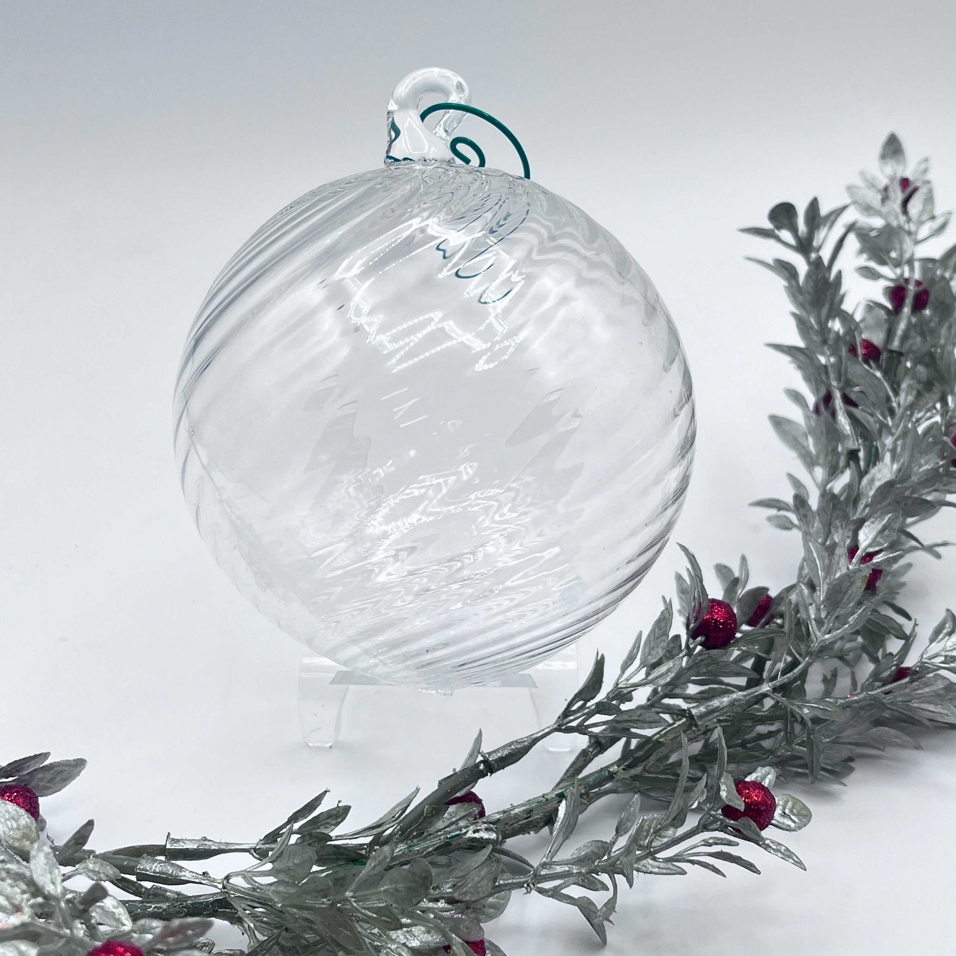 Clear hand blown glass ornament with spiral twist design, 4x4 inches, displayed with festive greenery and red berries.