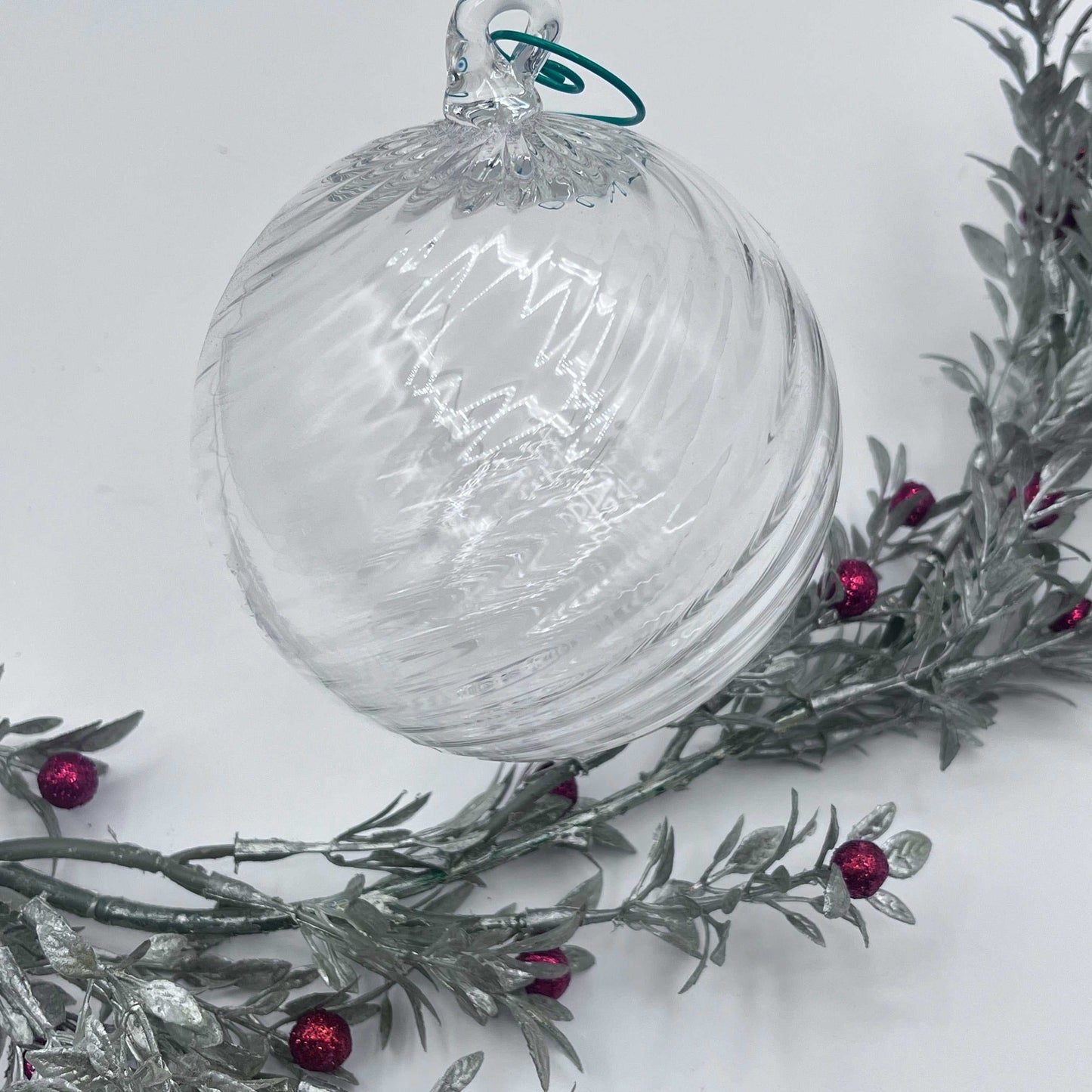 Clear blown glass ornament with spiral twist design hanging above silver branches with red berries