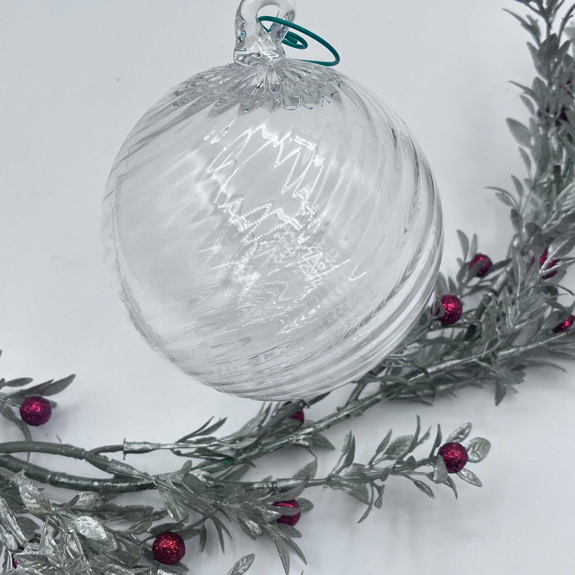 Clear blown glass ornament with spiral twist design hanging above silver branches with red berries