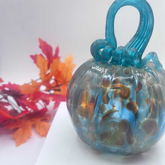Hand-blown art glass pumpkin in silver blue and gold with intricate swirled design and curled stem, autumn decor background