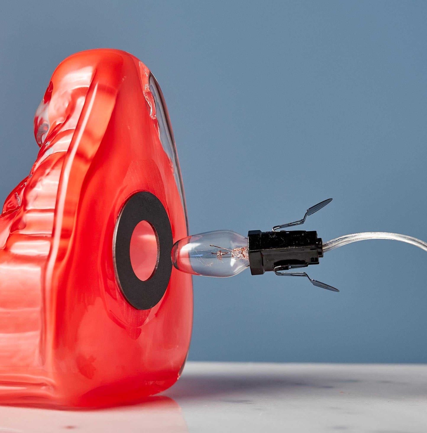 Red hand blown glass Buddha light with exposed bulb and black socket on blue background
