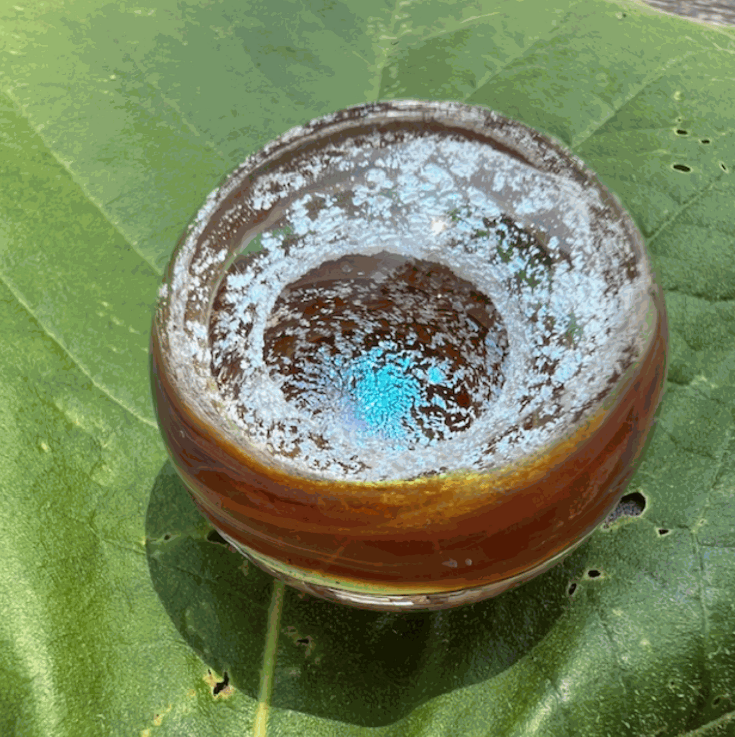 Ashes to Art Glass memorial paperweight orb with blue and amber colors on green leaf background