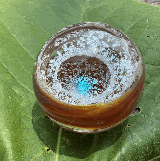Ashes to Art Glass memorial paperweight orb with blue and amber colors on green leaf background