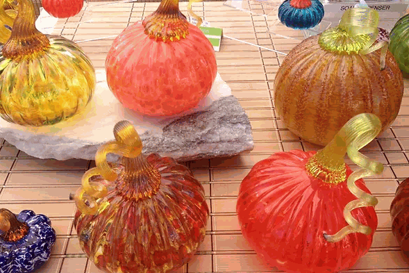Handcrafted colorful glass pumpkins displayed on a table, showcasing Make Your Own Pumpkin glassblowing class creations.