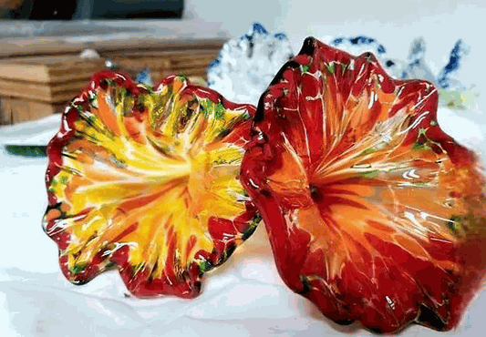 Colorful handmade glass flowers with vibrant red, yellow, and green hues displayed on a white surface
