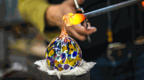 Glass artist shaping colorful blown glass ornament with torch at Holiday Glass Fest event