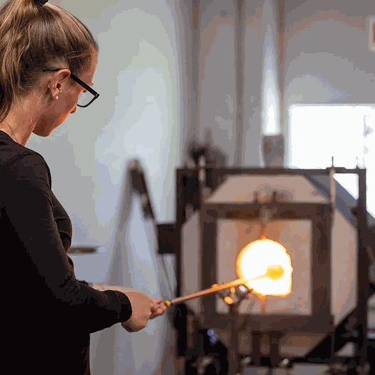 Woman participating in a 3 hr private glassblowing workshop heating glass in a furnace.
