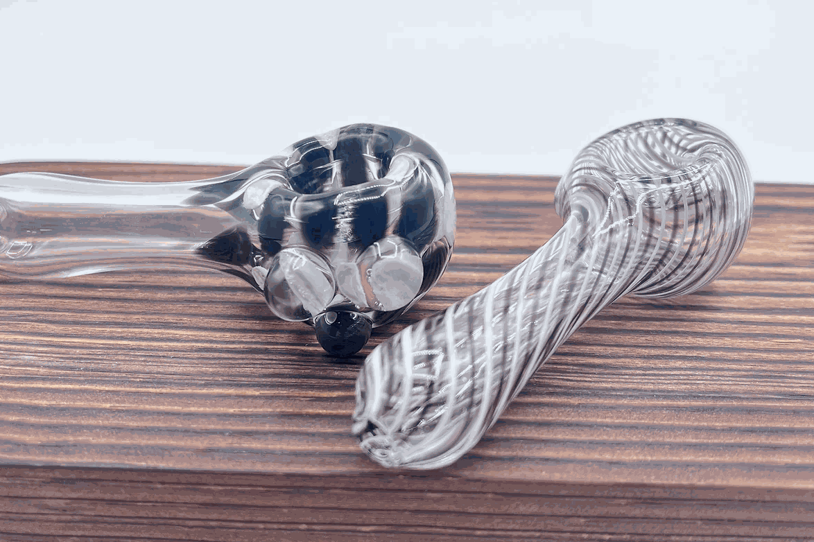 Two handcrafted clear glass flameworked pipes with black swirl designs on a wooden surface