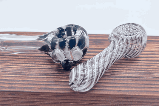 Two handcrafted clear glass flameworked pipes with black swirl designs on a wooden surface