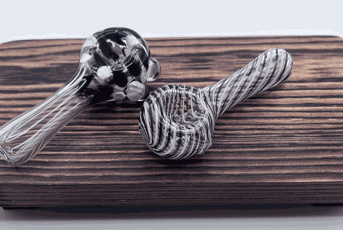 Two handmade flameworked glass pipes with intricate swirl and dot designs on a wooden display board.