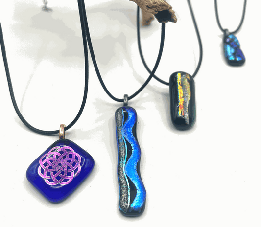 Handcrafted glass pendants with vibrant colors and unique designs on black cords, showcasing the Private Group Glass Experience.
