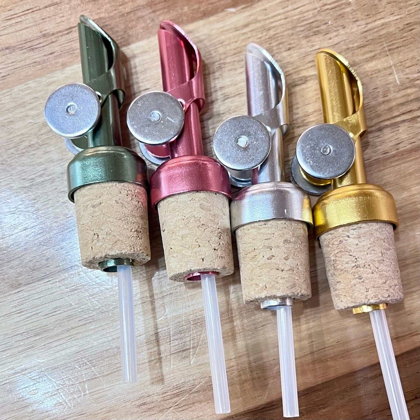 Colored weighted pour spouts with cork for olive oil and vinegar bottles in green, burgundy, silver, and gold colors.
