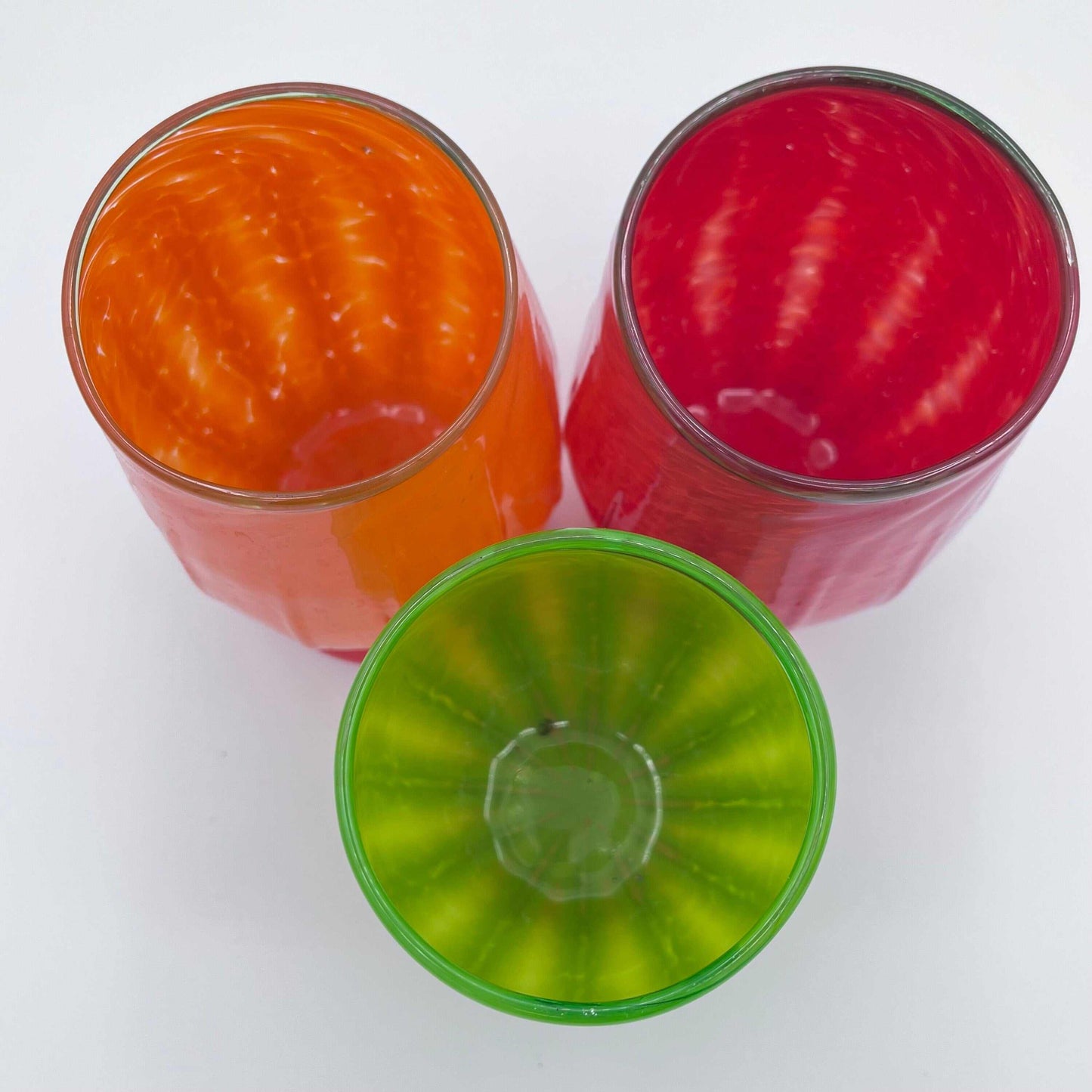 Top view of three colorful Gourdy Glasses stemless wine glasses in orange, red, and green colors, hand blown with textured autumn gourd-inspired design.