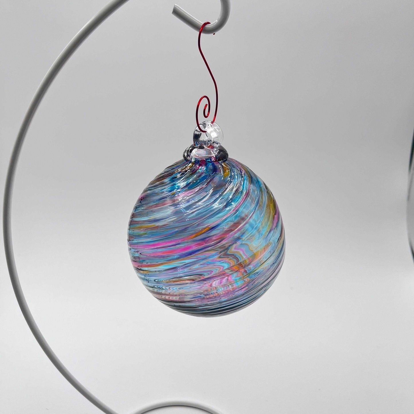 Hand blown glass holiday ornament with colorful bluesy spiral twist design hanging on metal stand