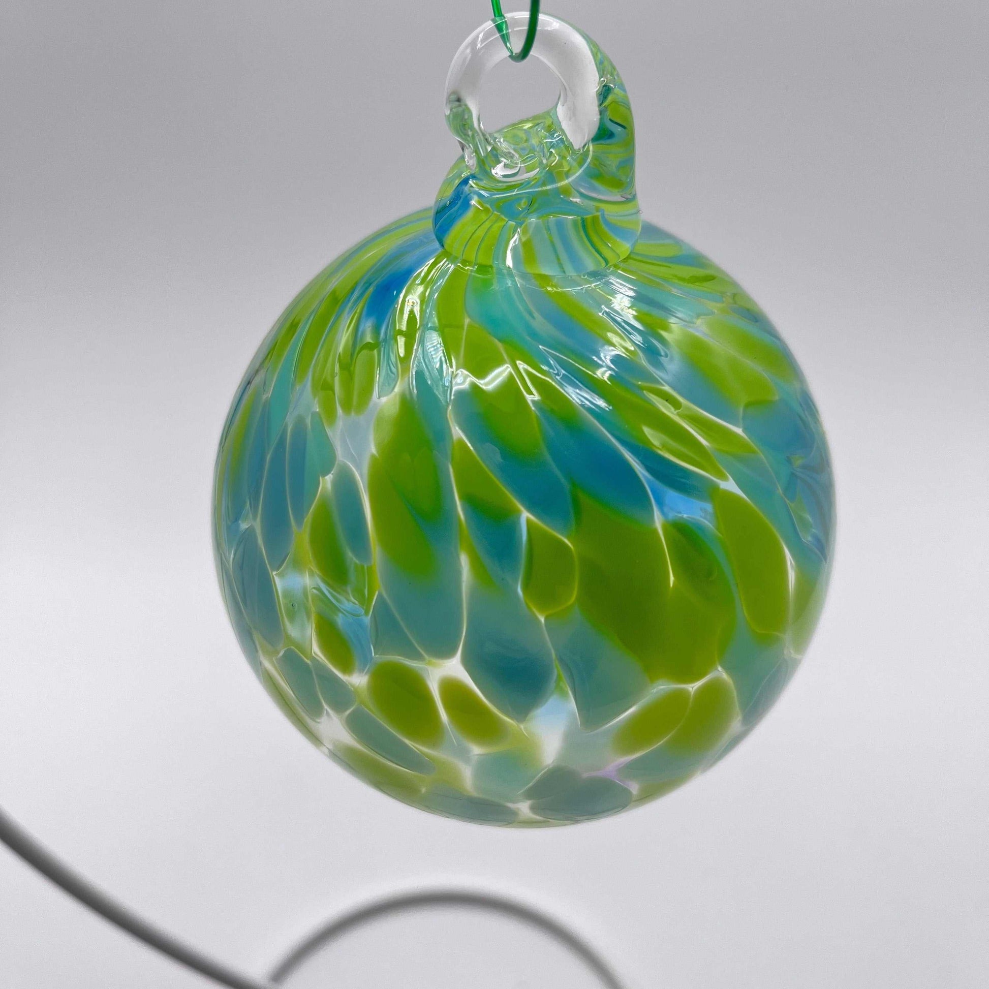 Green and blue speckled hand blown glass ornament hanging on a clear loop