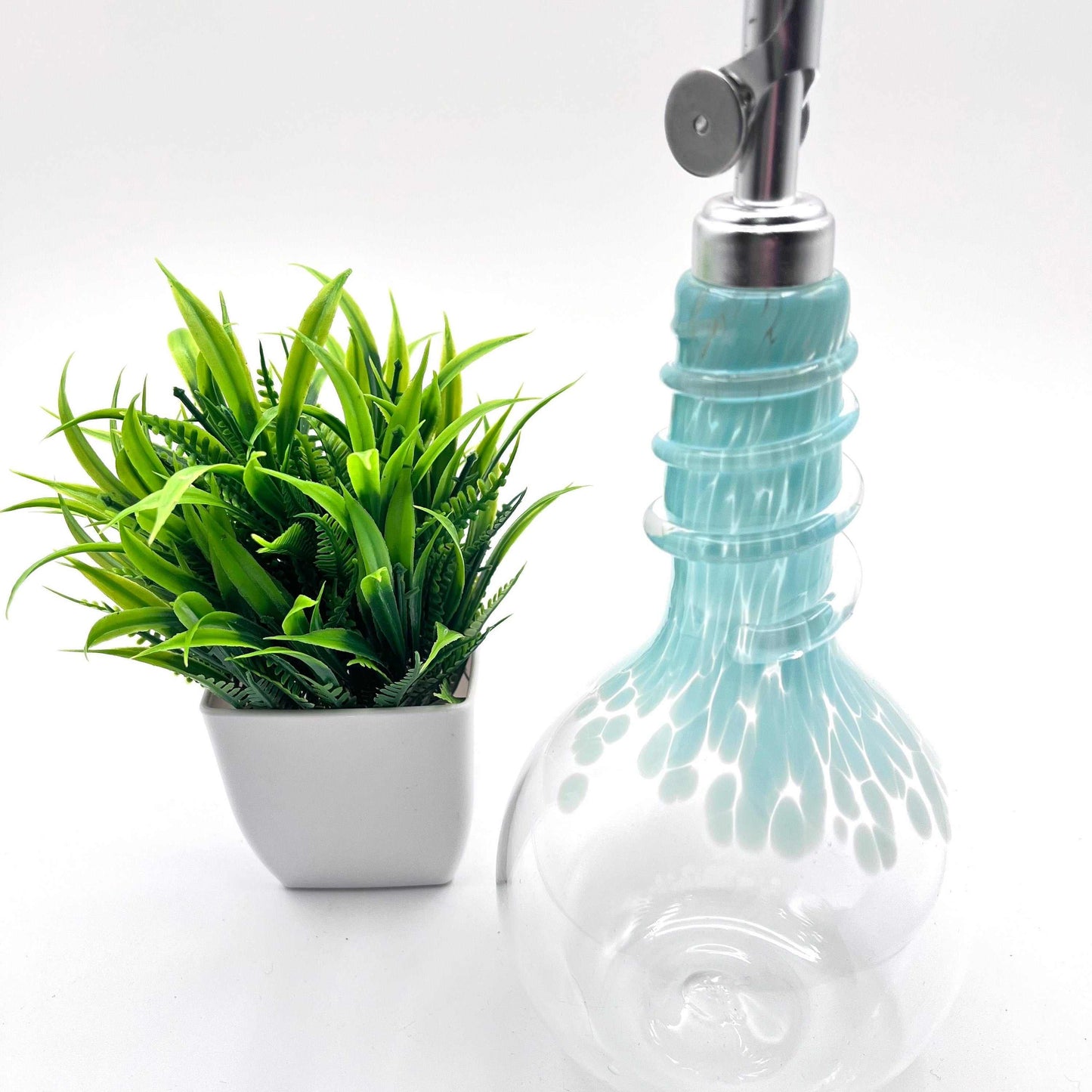 Celadon glass oil and vinegar drizzler bottle with spiral neck and weighted spout next to small green plant