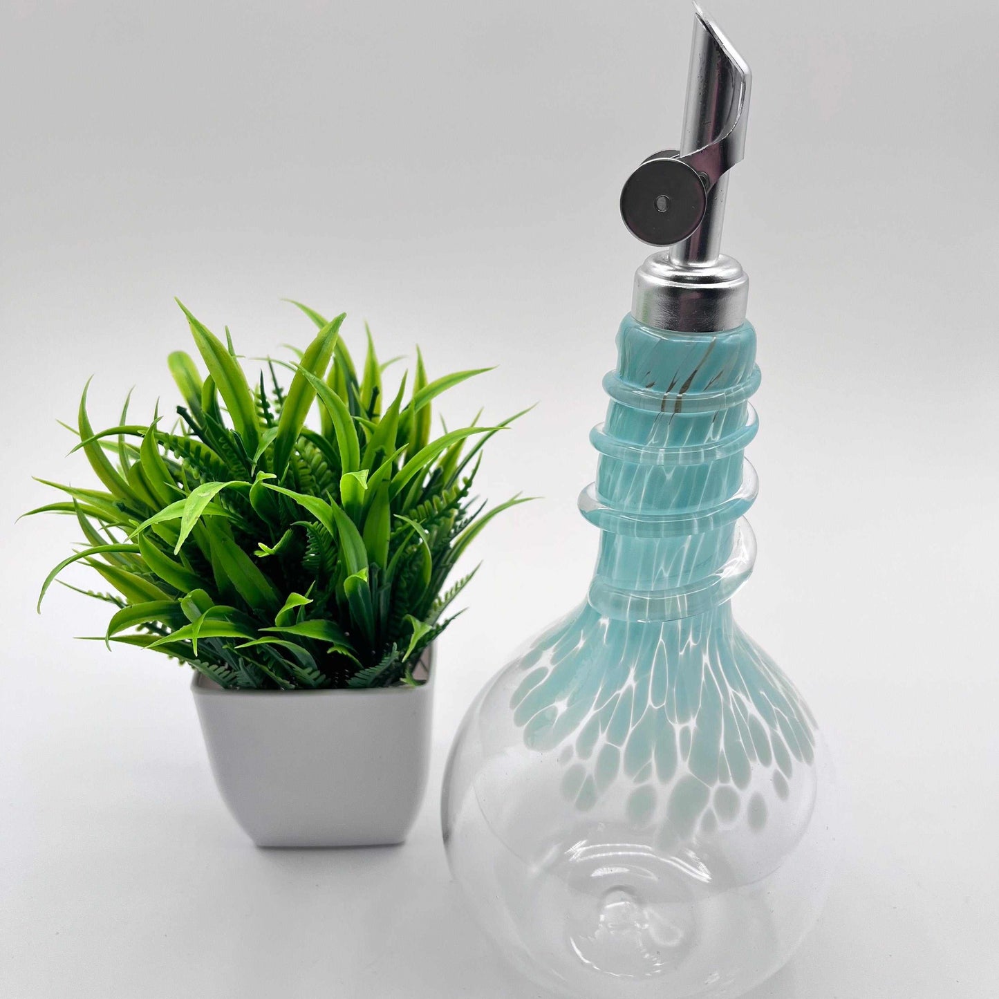 Celadon oil and vinegar spiral neck drizzler cruet bottle with weighted pour spout and unique hand-blown design next to small green plant