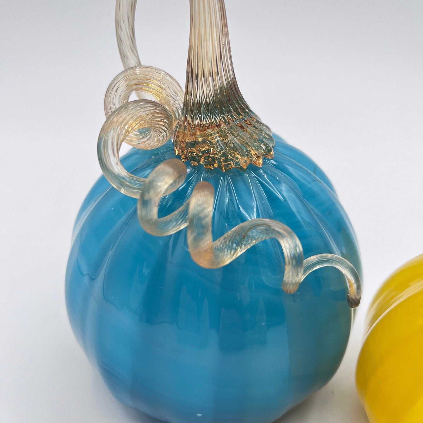 Set of two hand blown glass pumpkins with curly stems, one blue and one yellow, handcrafted by Blackstone River Glass Center.